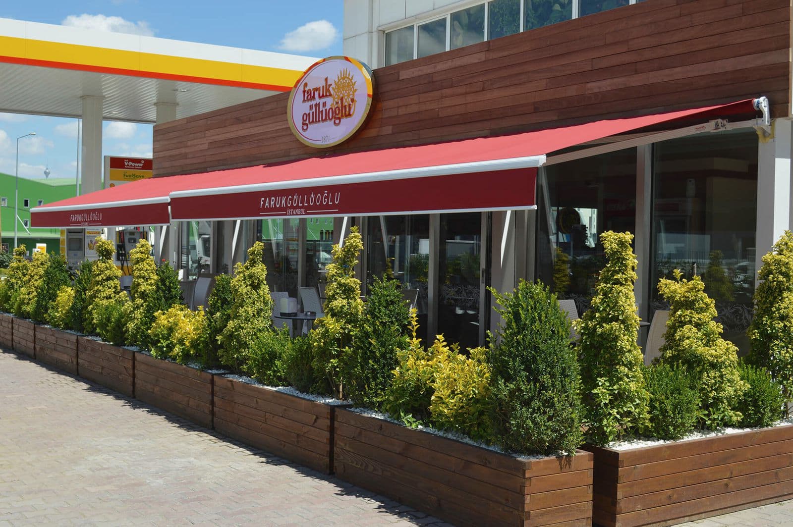 Kafe önünde açık kırmızı mafsallı tenteler ve saksı bitkileri