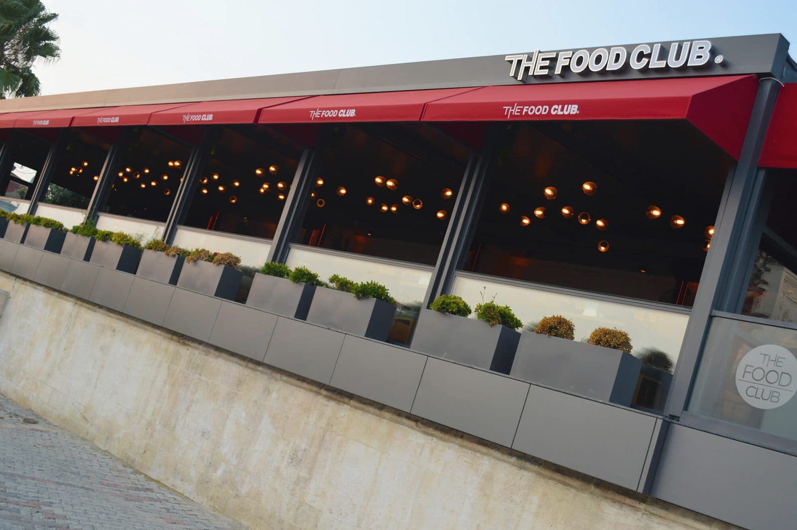 Restoran cephesi boyunca logolu kırmızı mimari tenteler, yan görünüş