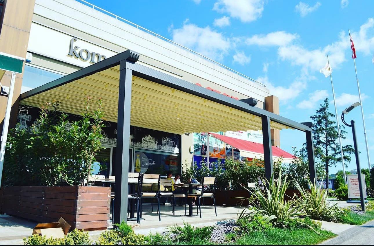 Restoran terasında antrasit alüminyum profilli, krem blackout kumaş tavanlı Pergola Sistem